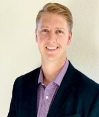 A man in a suit is smiling in front of a white wall.